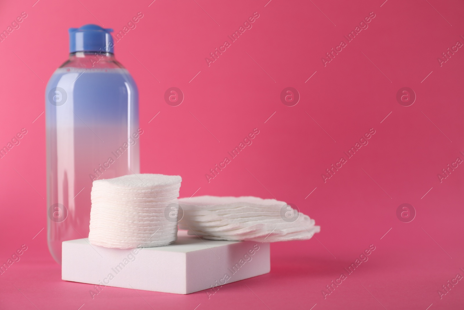 Photo of Clean cotton pads and micellar water on pink background. Space for text