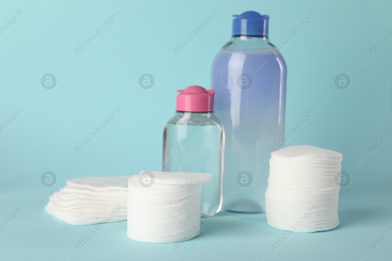 Photo of Clean cotton pads and micellar water on light blue background. Space for text