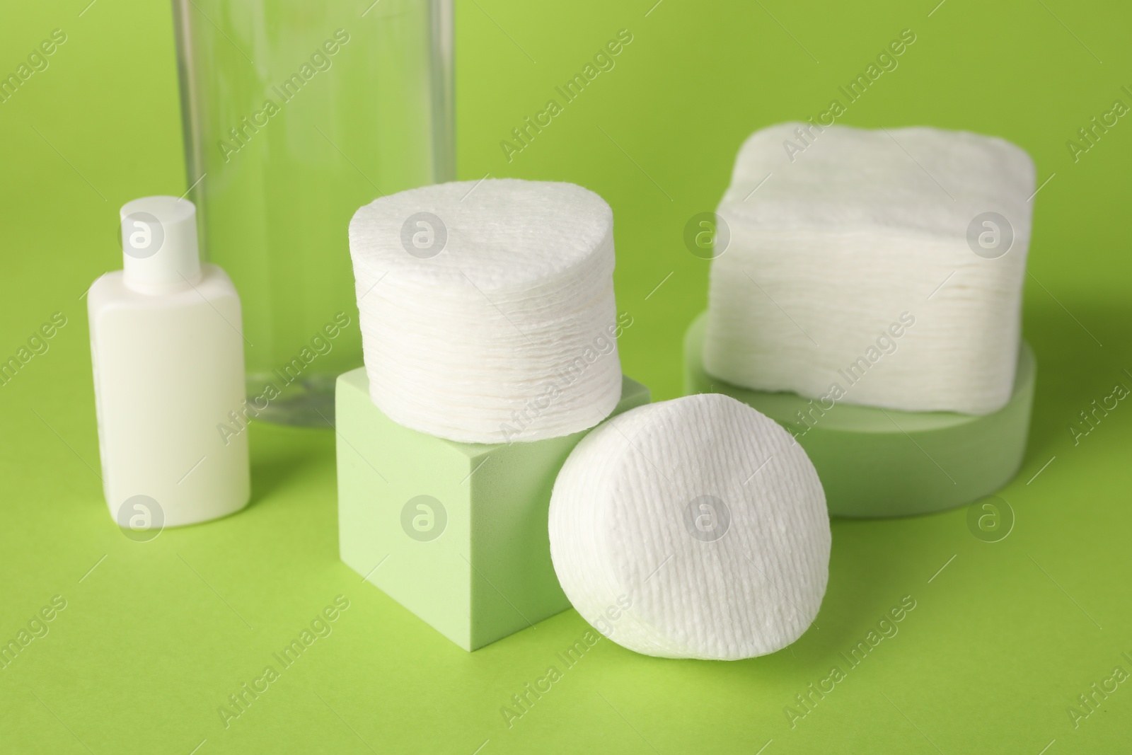 Photo of Clean cotton pads and cosmetic products on green background, closeup