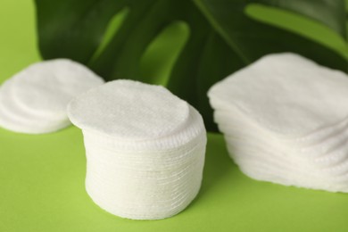 Photo of Clean cotton pads and leaf on green background, closeup