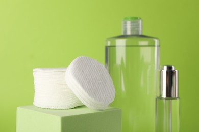 Photo of Clean cotton pads and cosmetic products on green background, closeup