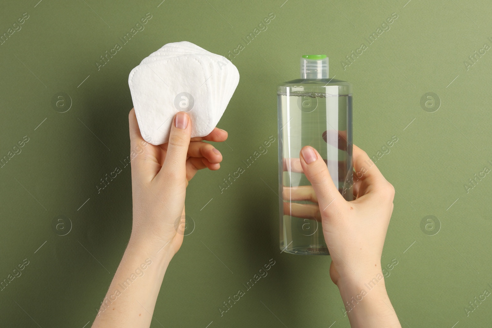 Photo of Woman with micellar water and clean cotton pads on olive background, closeup