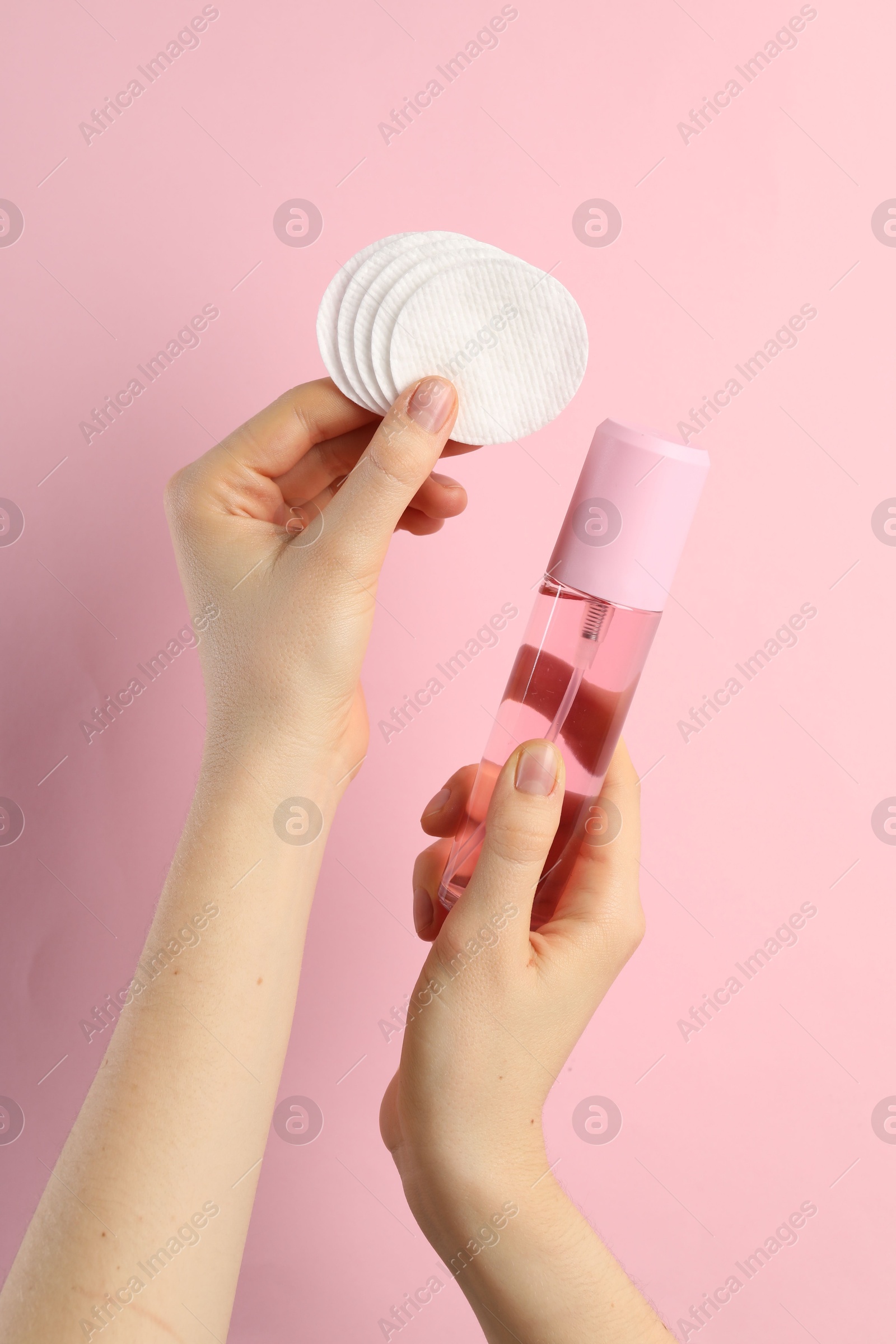 Photo of Woman with micellar water and clean cotton pads on light pink background, closeup