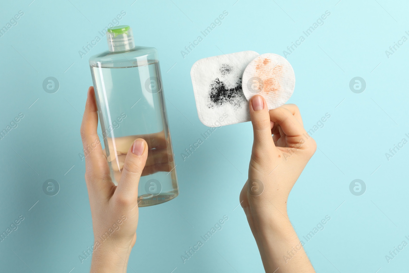 Photo of Woman with micellar water and dirty cotton pads on light blue background, closeup