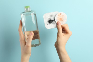 Photo of Woman with micellar water and dirty cotton pads on light blue background, closeup