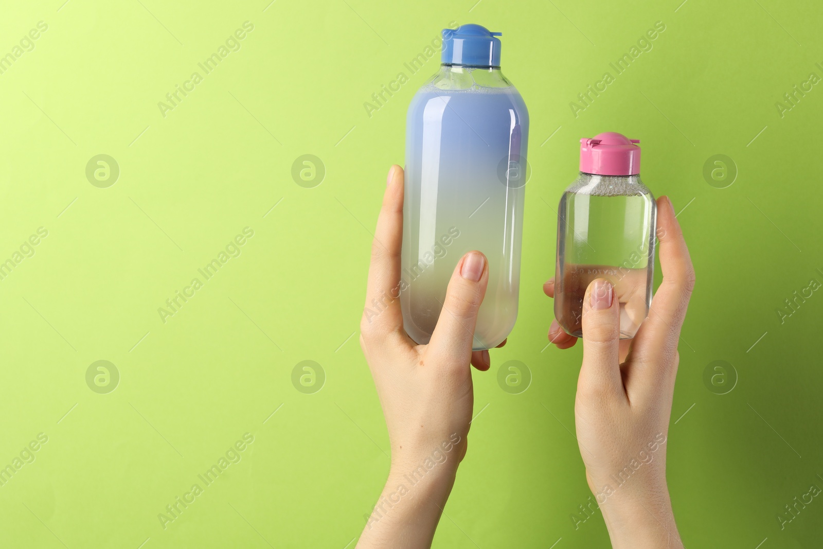 Photo of Woman with bottles of cosmetic products on green background, closeup