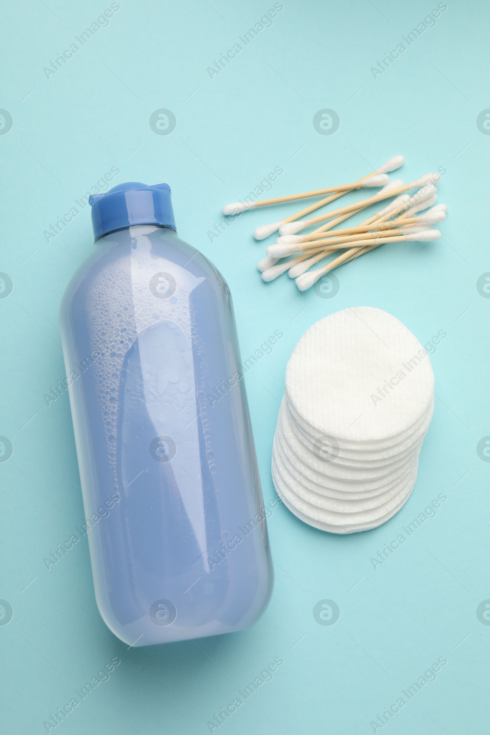 Photo of Clean cotton pads, swabs and micellar water on light blue background, flat lay