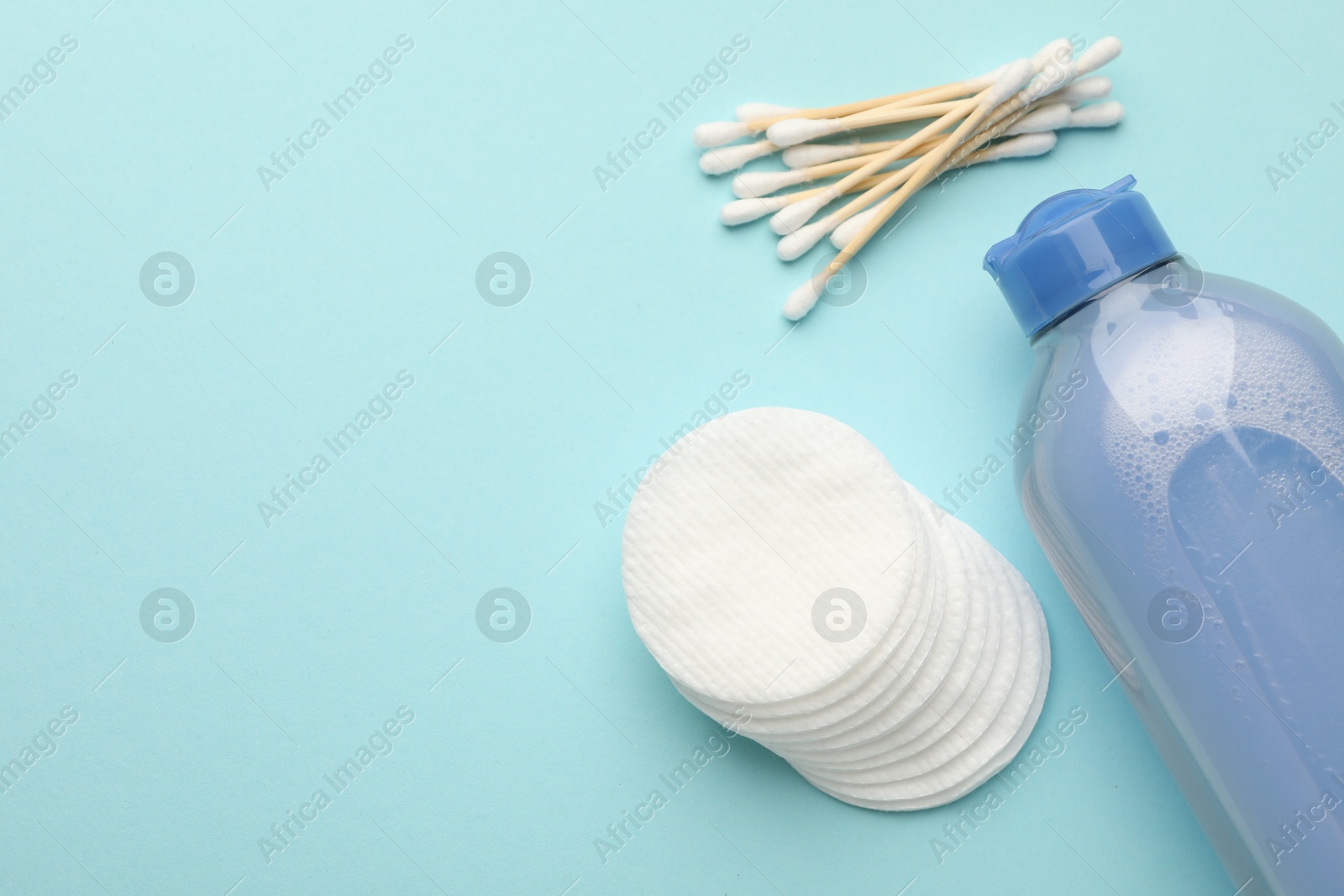 Photo of Clean cotton pads, swabs and micellar water on light blue background, flat lay. Space for text