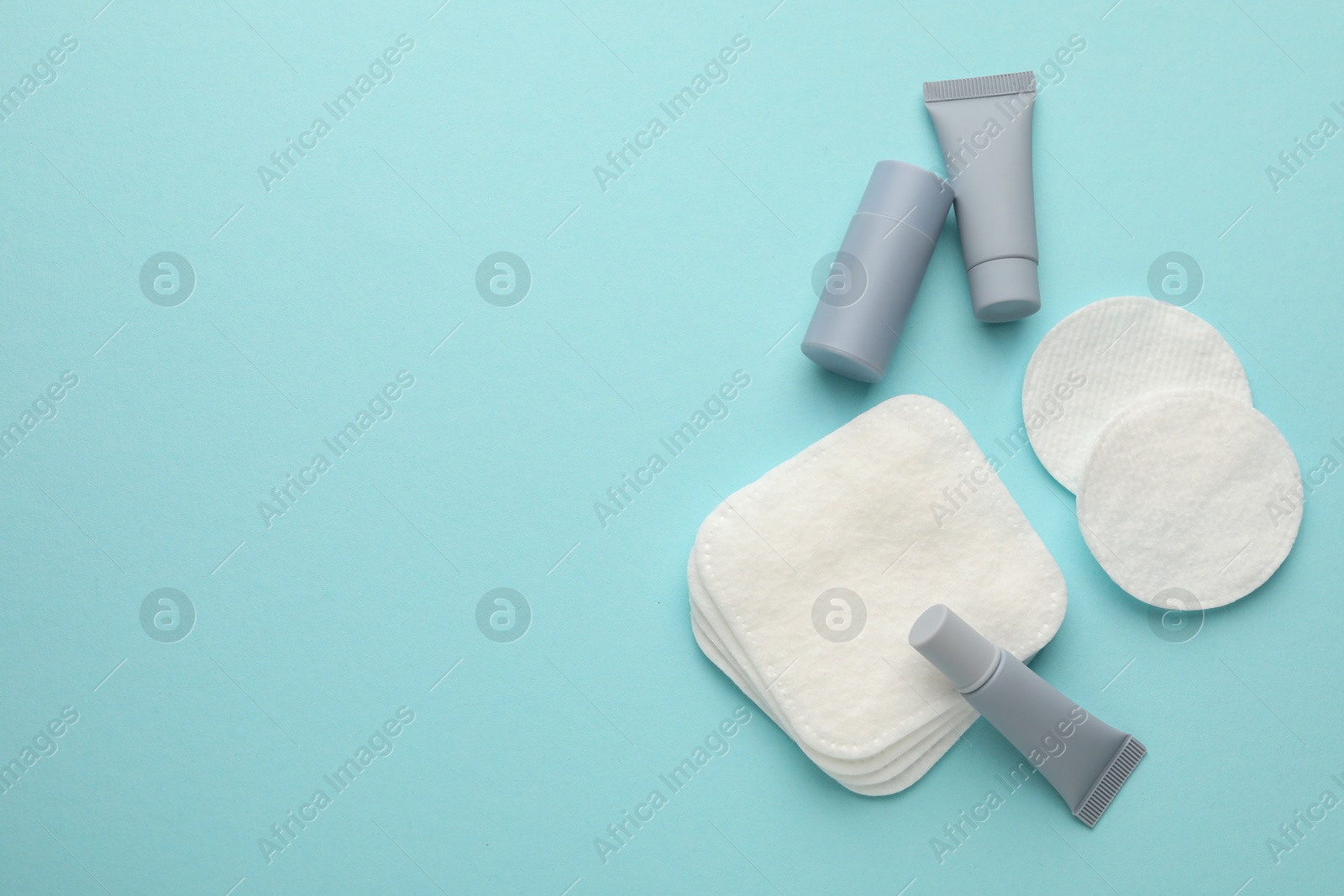 Photo of Clean cotton pads and cosmetic products on light blue background, flat lay. Space for text