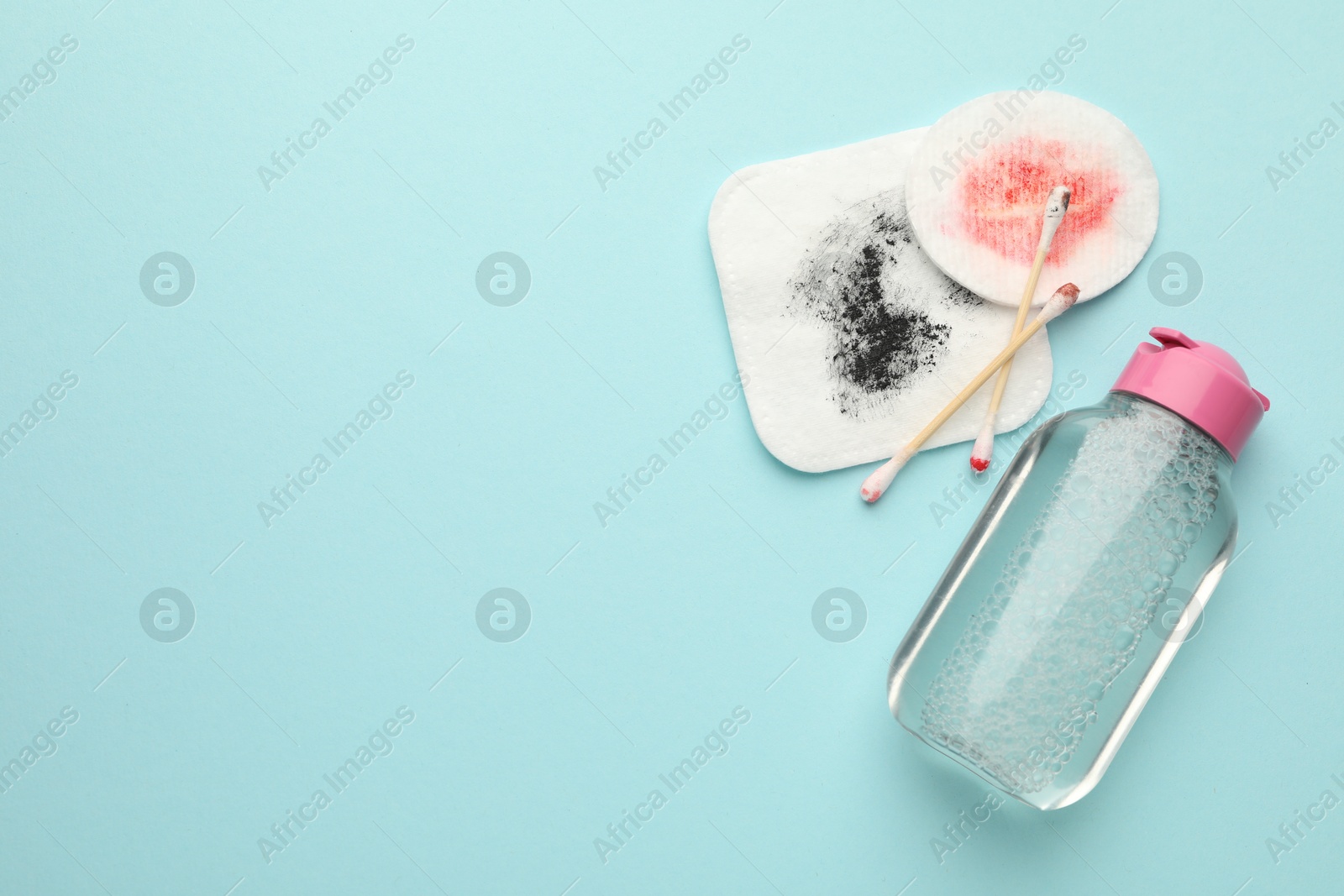 Photo of Dirty cotton pads, swabs and micellar water on light blue background, top view. Space for text