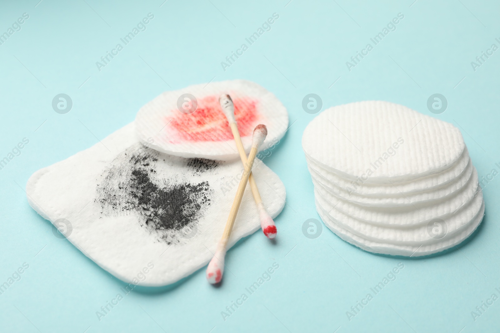 Photo of Clean and dirty cotton pads with swabs on light blue background, closeup