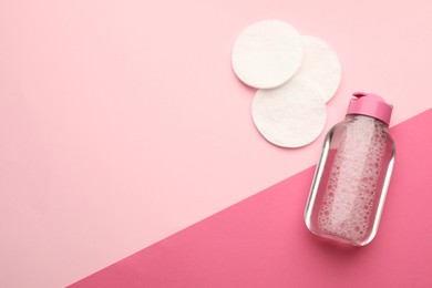 Photo of Clean cotton pads and micellar water on pink background, flat lay. Space for text