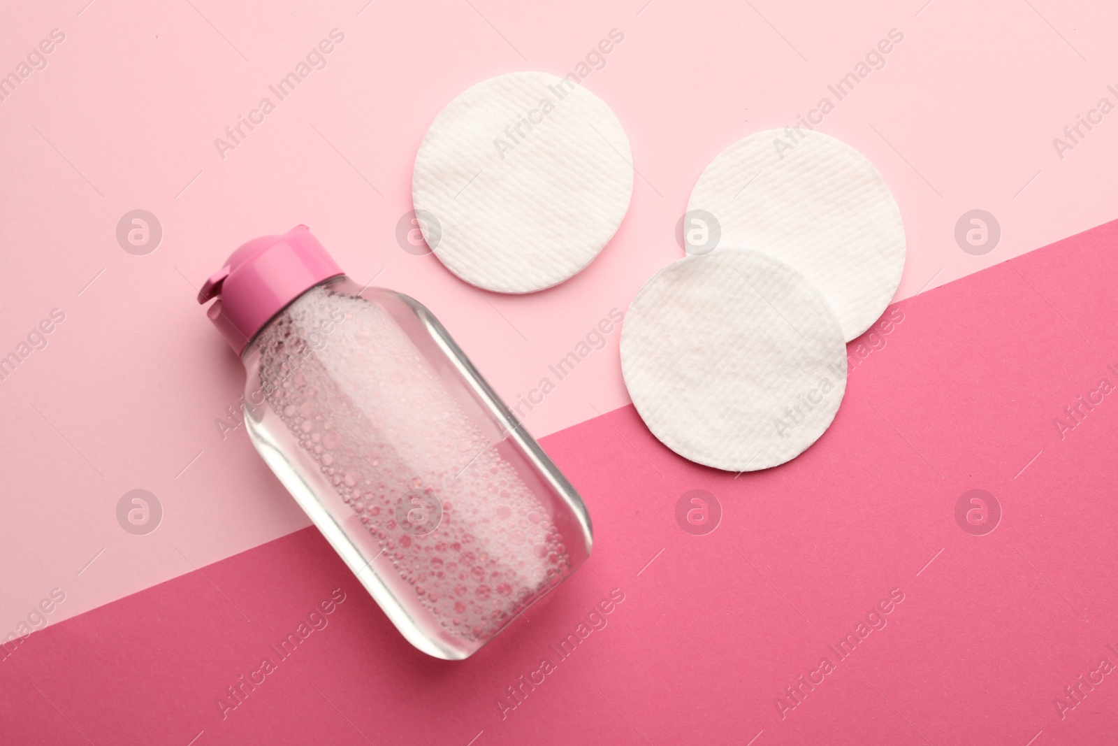 Photo of Clean cotton pads and micellar water on pink background, flat lay