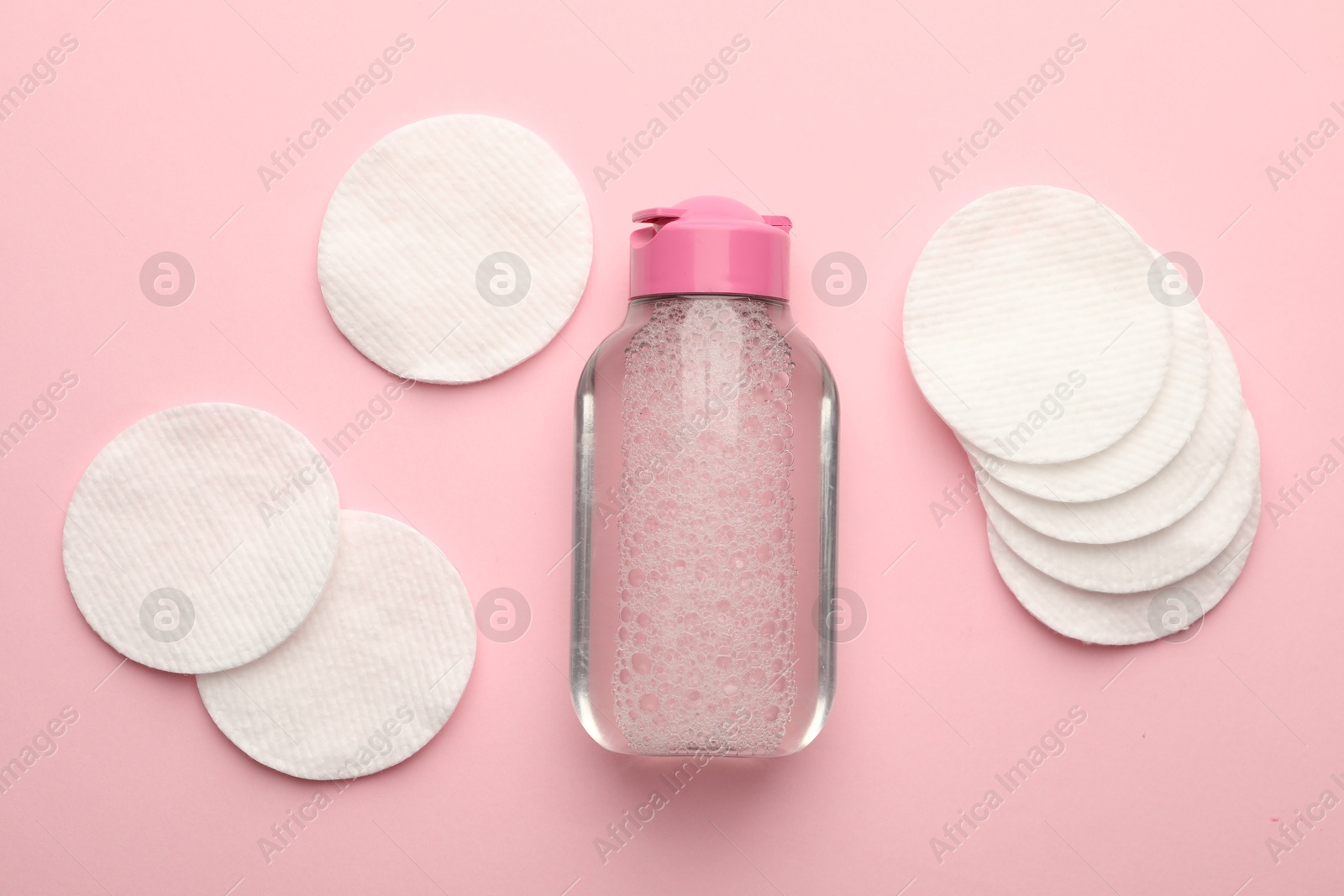 Photo of Clean cotton pads and micellar water on pink background, flat lay