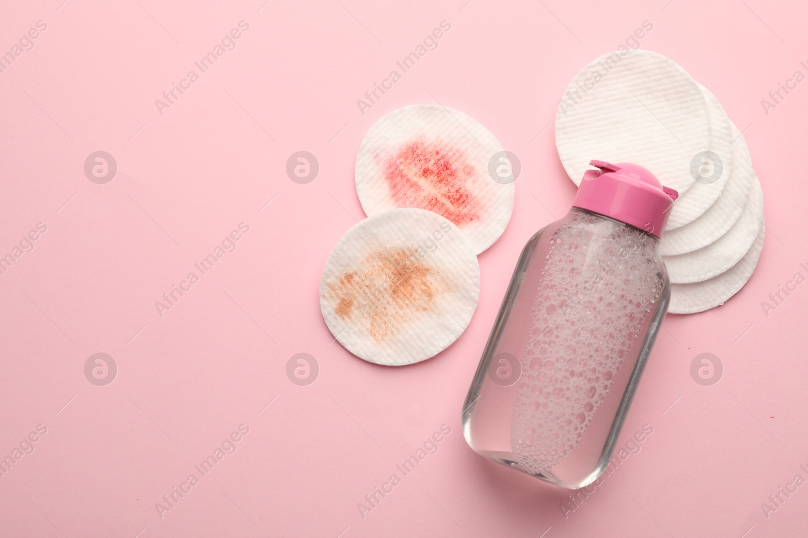 Photo of Clean and dirty cotton pads with micellar water on pink background, flat lay. Space for text