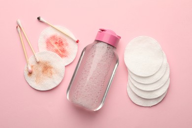 Photo of Clean and dirty cotton pads, swabs with micellar water on pink background, flat lay