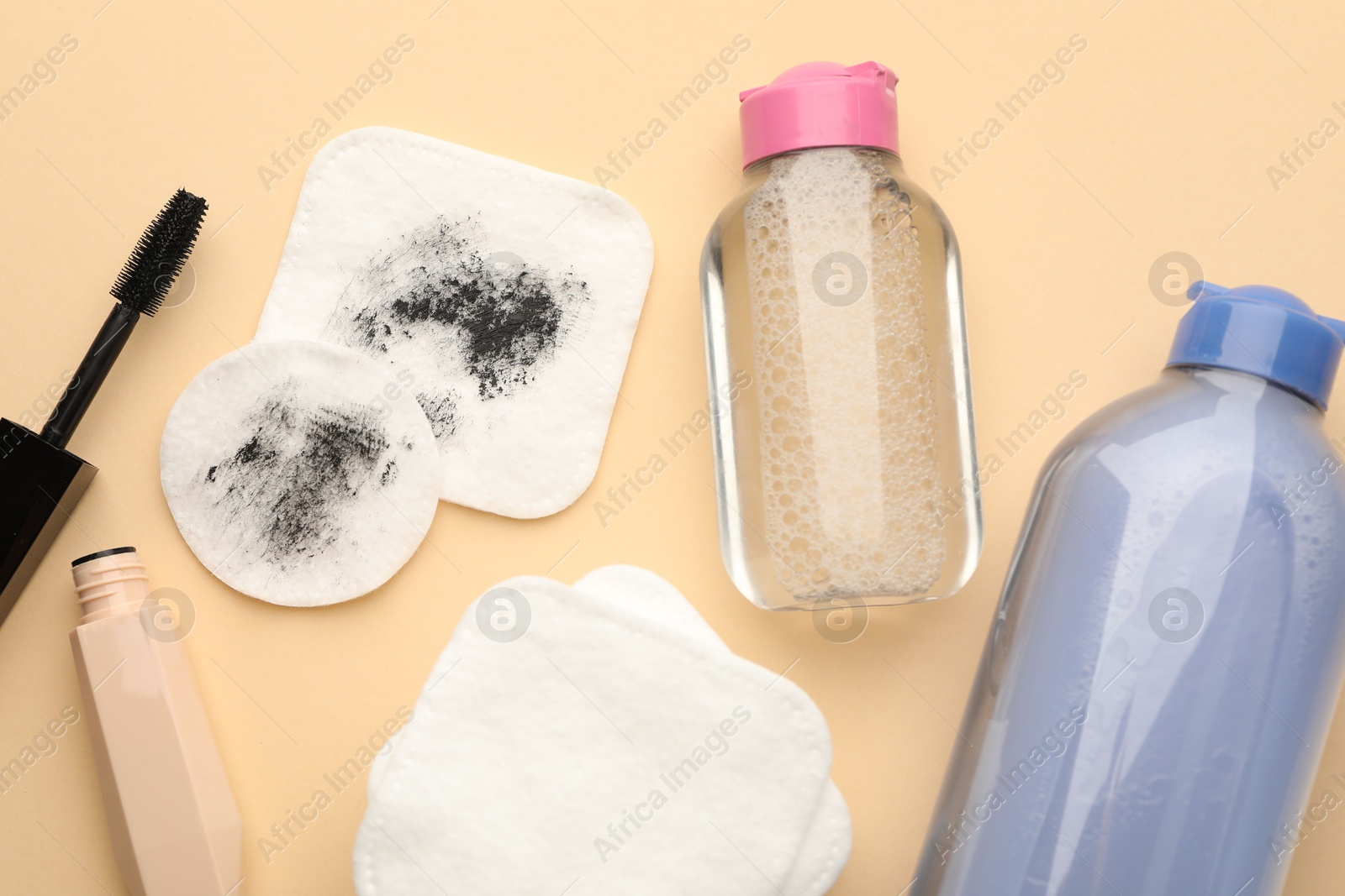 Photo of Clean and dirty cotton pads, mascara, micellar water on beige background, flat lay