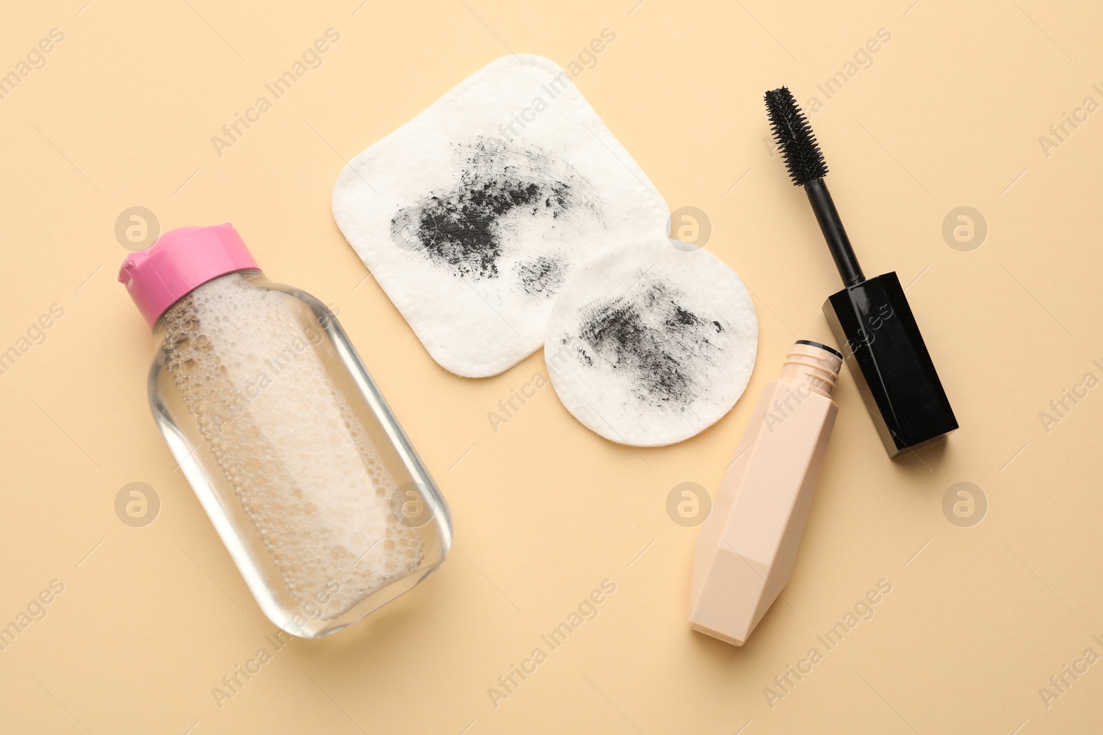 Photo of Dirty cotton pads, mascara and micellar water on beige background, flat lay