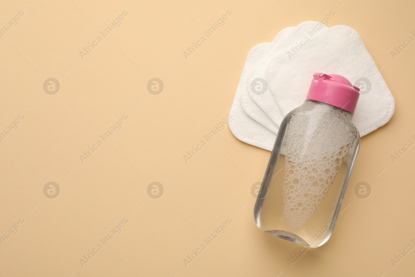 Photo of Clean cotton pads and micellar water on beige background, top view. Space for text