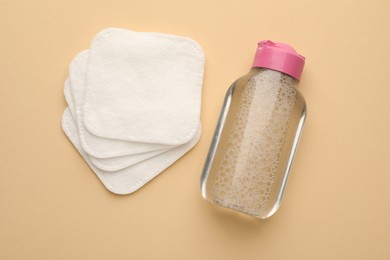 Clean cotton pads and micellar water on beige background, top view