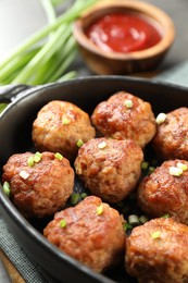 Photo of Tasty meatballs with green onion in baking dish on table, closeup