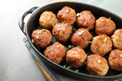 Photo of Tasty meatballs with green onion in baking dish on grey table, closeup