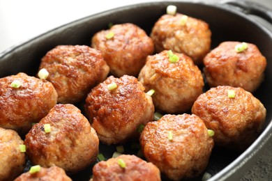 Photo of Tasty meatballs with green onion in baking dish on table, closeup