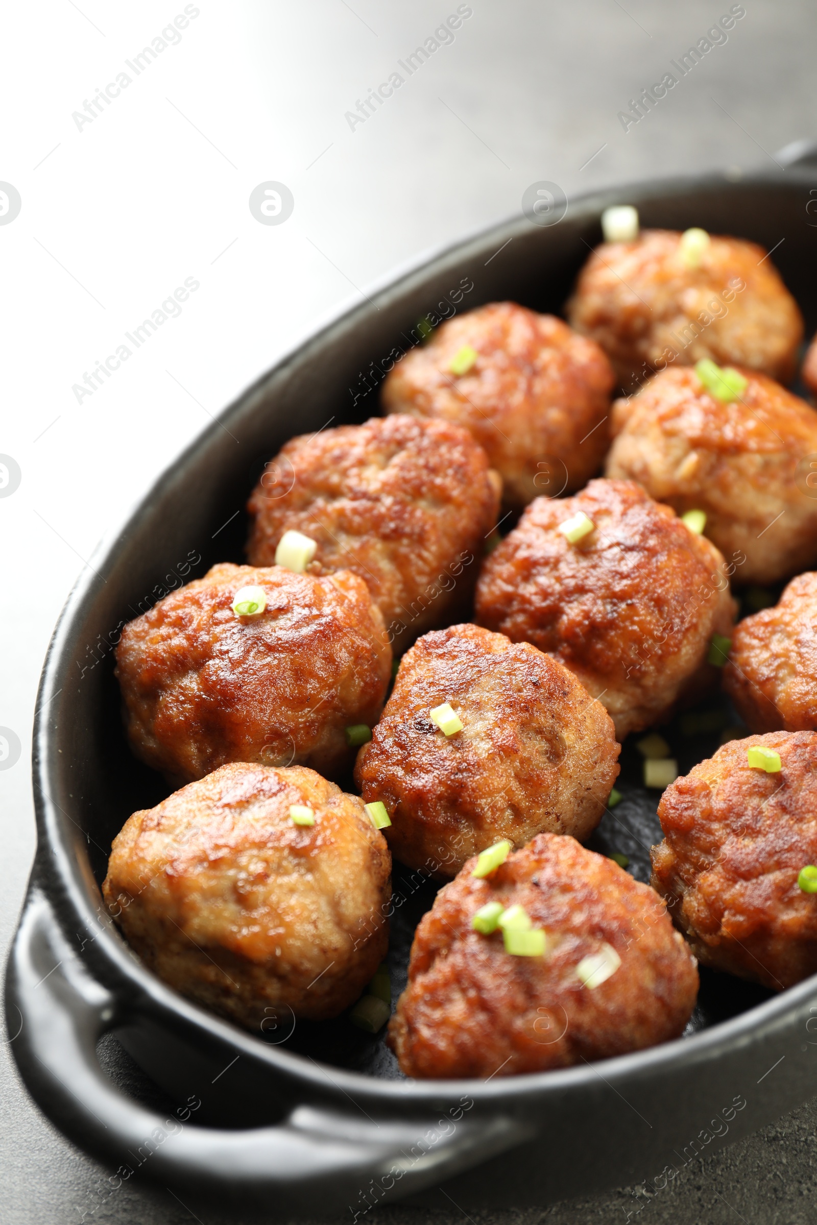 Photo of Tasty meatballs with green onion in baking dish on grey table, closeup