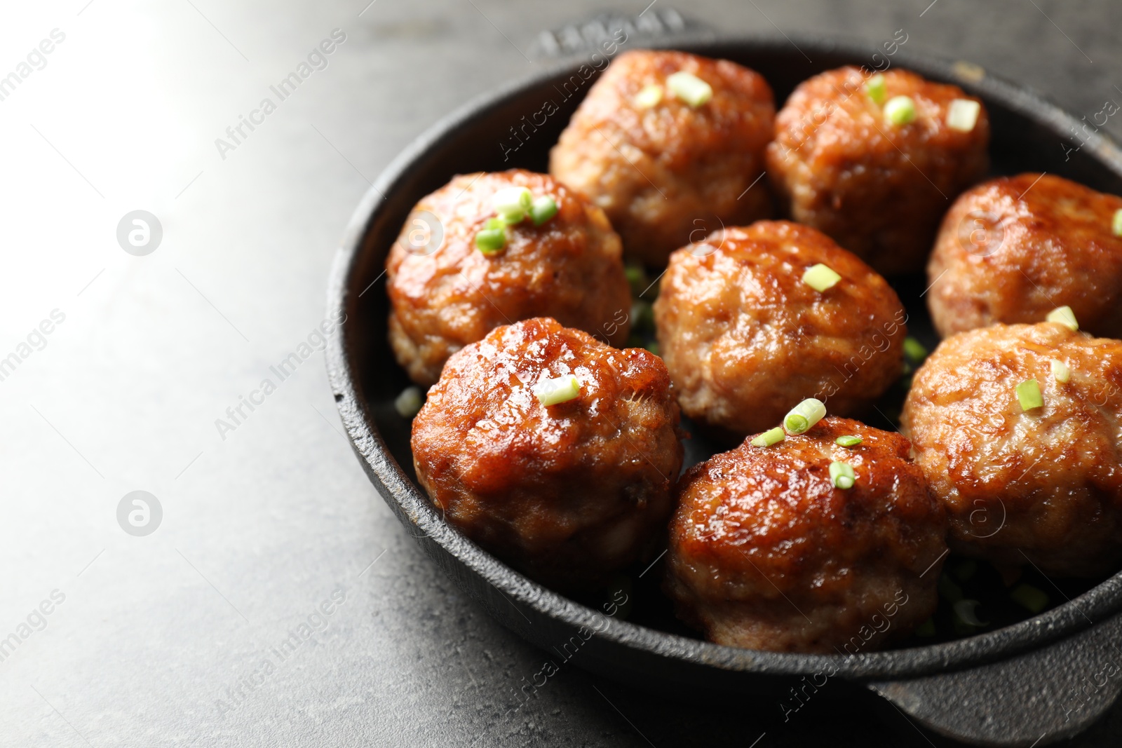 Photo of Tasty meatballs with green onion in baking dish on grey table, closeup