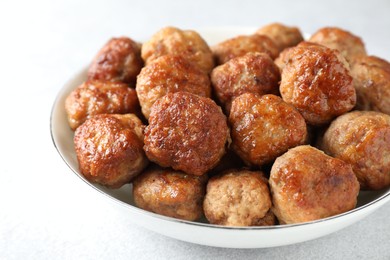 Photo of Tasty cooked meatballs in bowl on white table, closeup