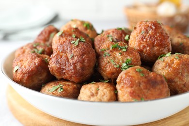 Photo of Tasty cooked meatballs with green onion in bowl on white table, closeup