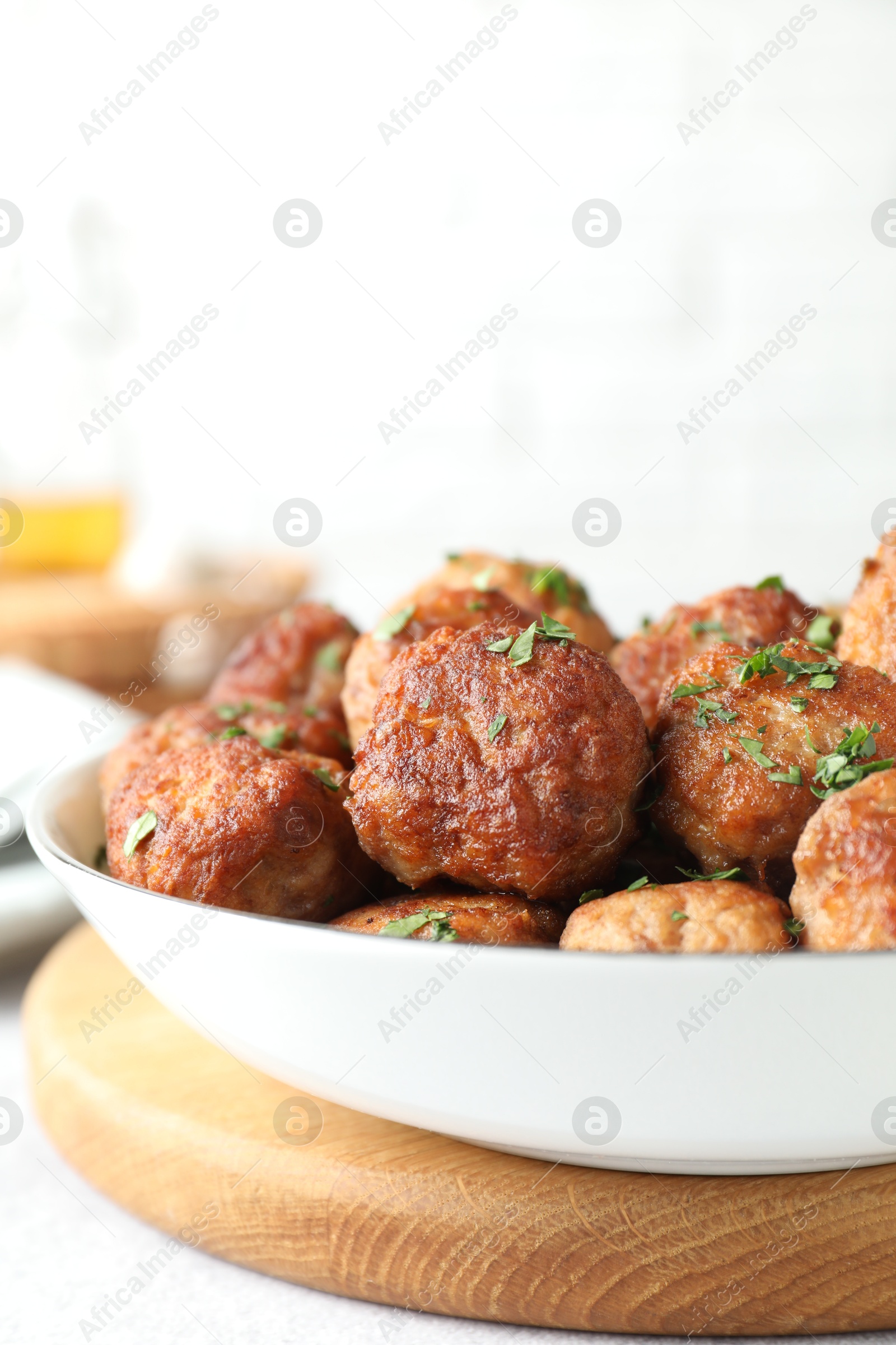 Photo of Tasty cooked meatballs with green onion in bowl on white table, closeup