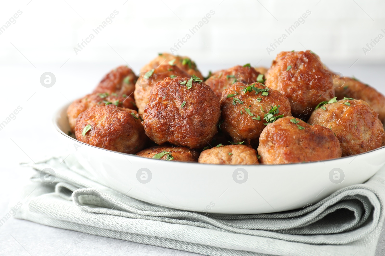 Photo of Tasty cooked meatballs with green onion in bowl on white table, closeup