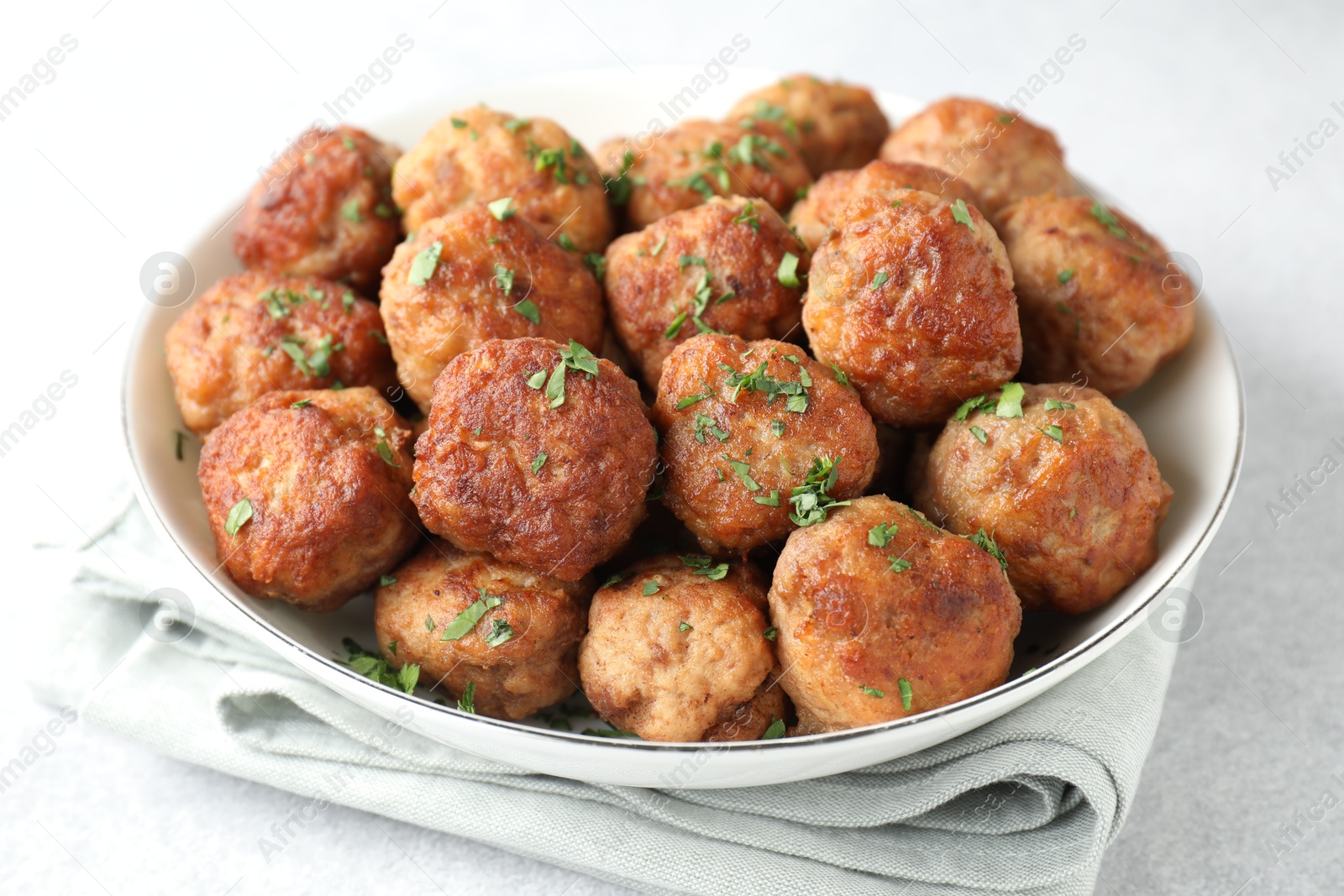 Photo of Tasty cooked meatballs with green onion in bowl on white table, closeup