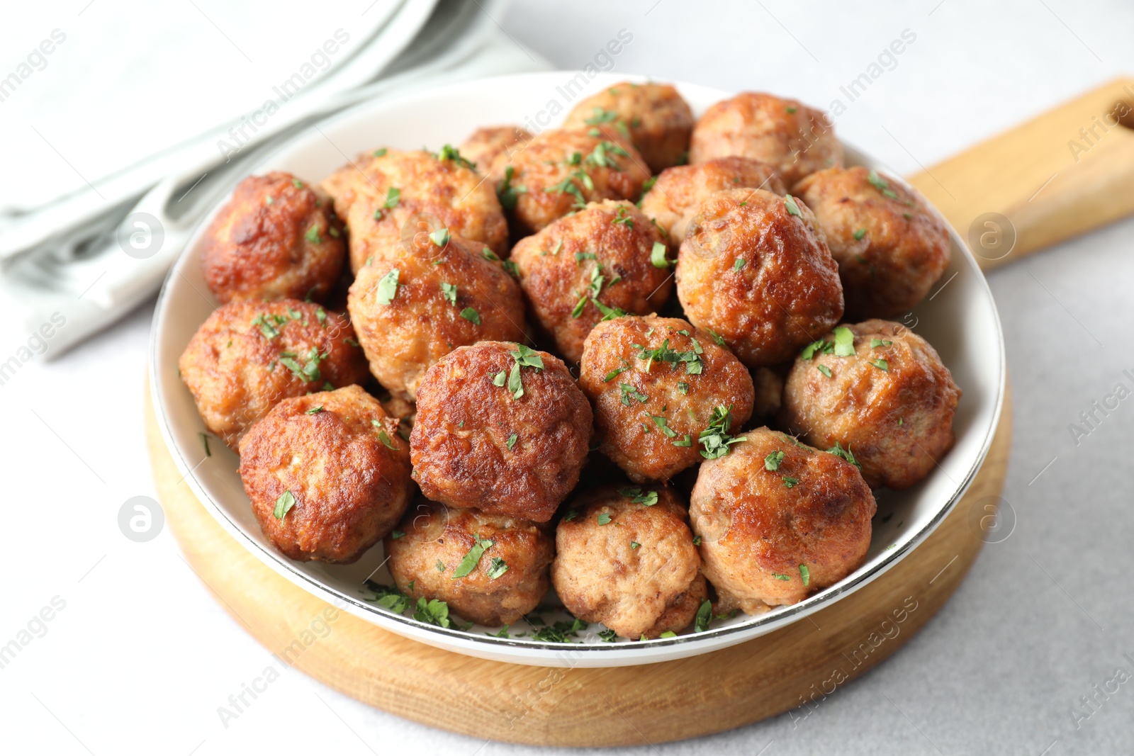 Photo of Tasty cooked meatballs with green onion in bowl on white table, closeup