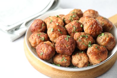 Photo of Tasty cooked meatballs with green onion in bowl on white table, closeup