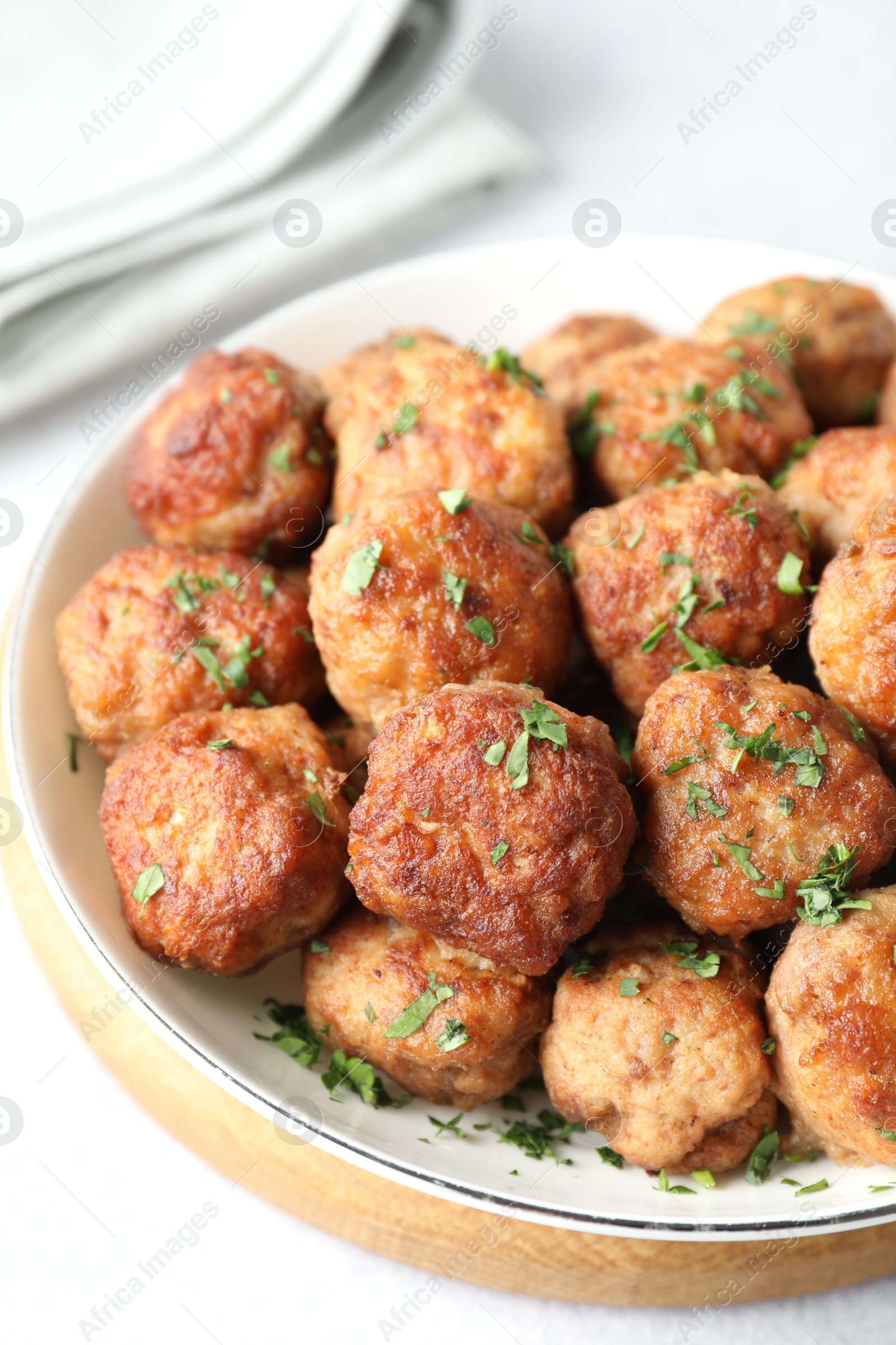 Photo of Tasty cooked meatballs with green onion in bowl on white table, closeup