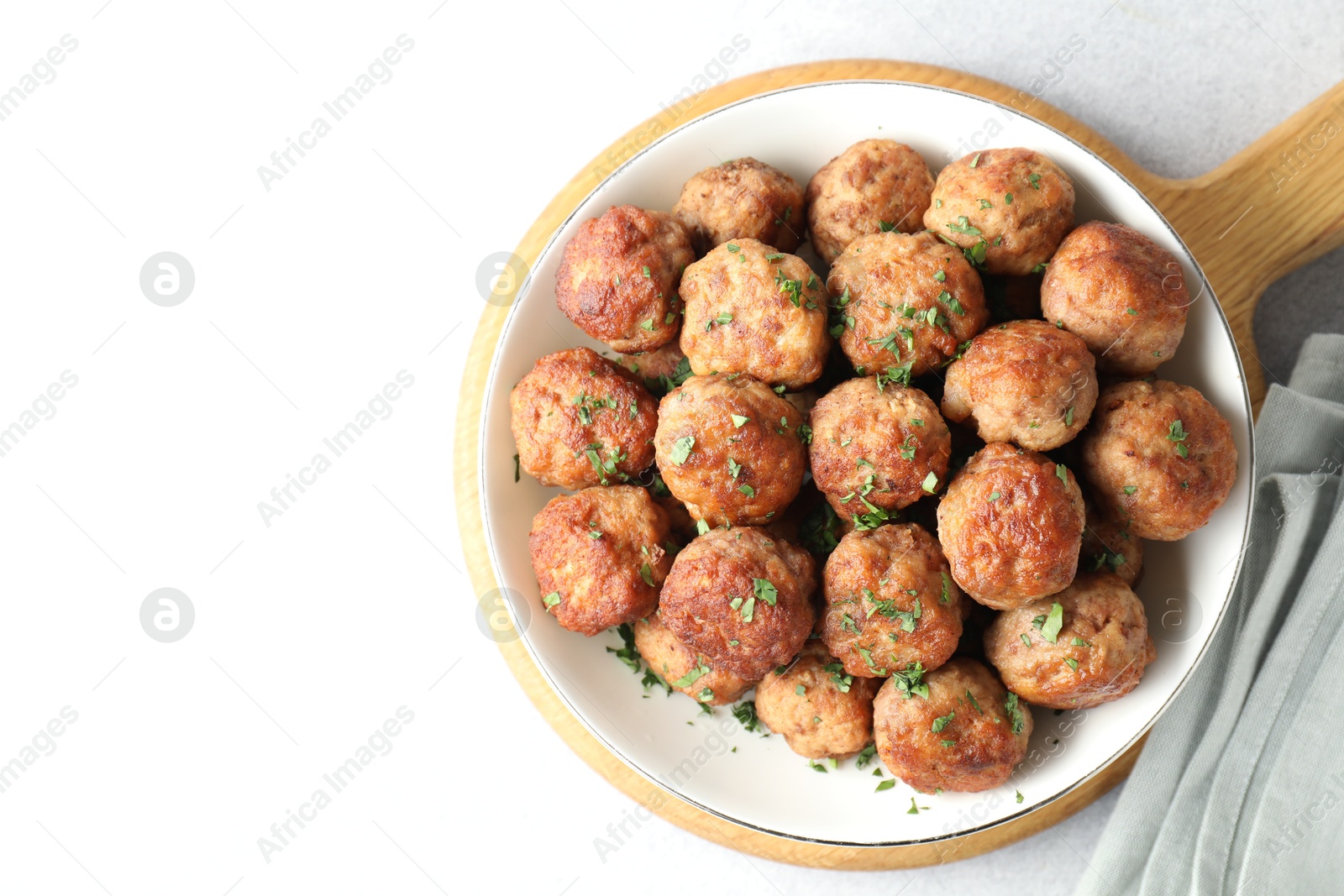 Photo of Tasty cooked meatballs with green onion in bowl on white table, top view. Space for text