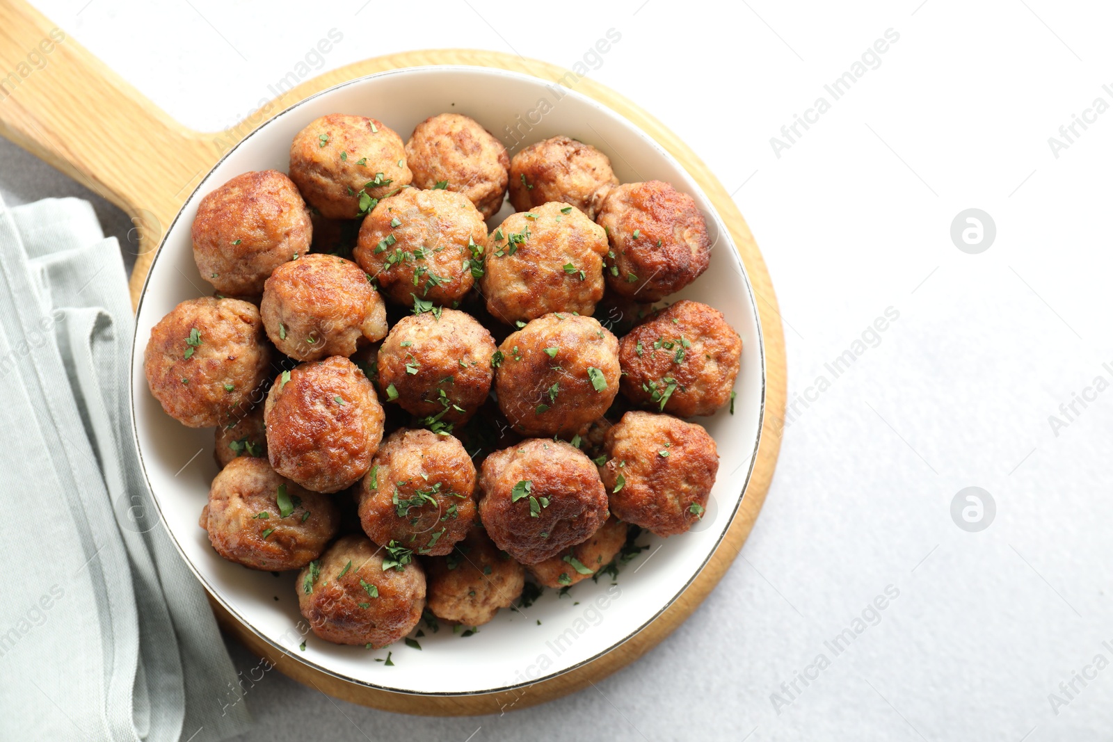 Photo of Tasty cooked meatballs with green onion in bowl on white table, top view. Space for text