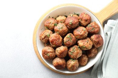 Photo of Tasty cooked meatballs with green onion in bowl on white table, top view. Space for text