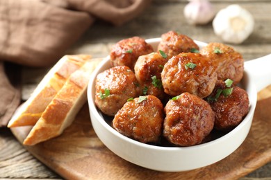 Photo of Tasty meatballs with green onion in baking dish and bread pieces on wooden table, closeup