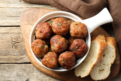 Photo of Tasty meatballs with green onion in baking dish and bread pieces on wooden table, flat lay