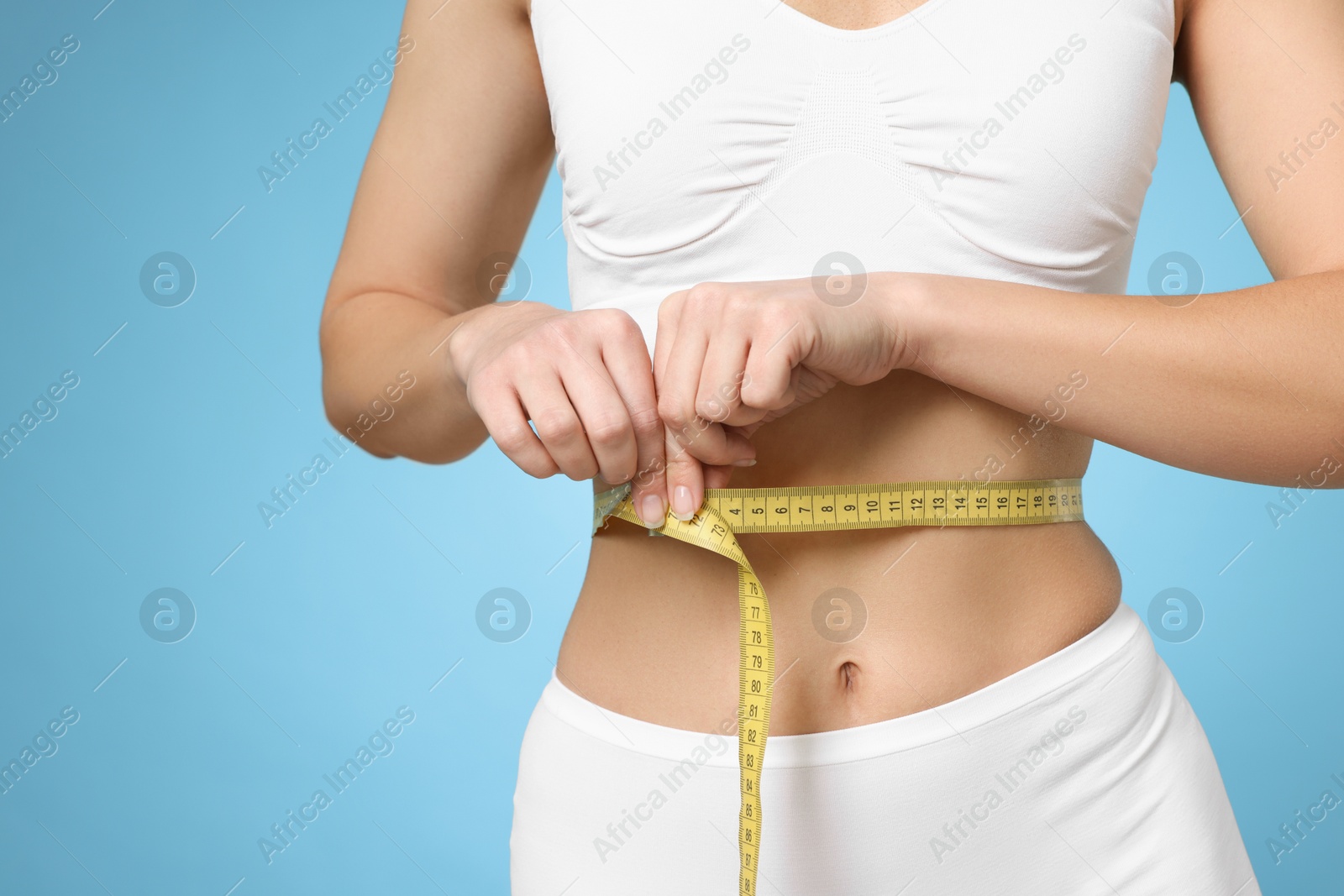 Photo of Weight loss. Woman measuring her slim waist with tape on light blue background, closeup