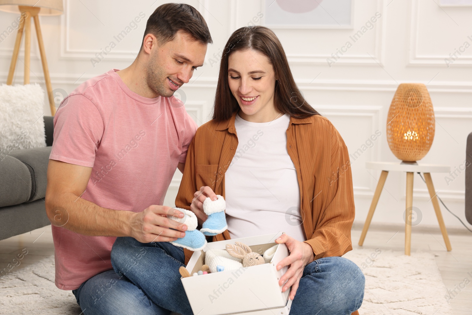 Photo of Pregnant woman and her husband with box of baby toys and booties at home