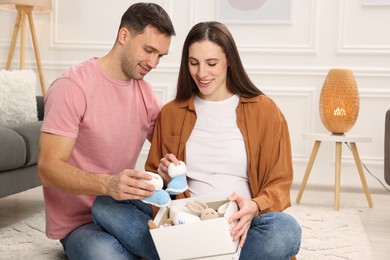 Photo of Pregnant woman and her husband with box of baby toys and booties at home