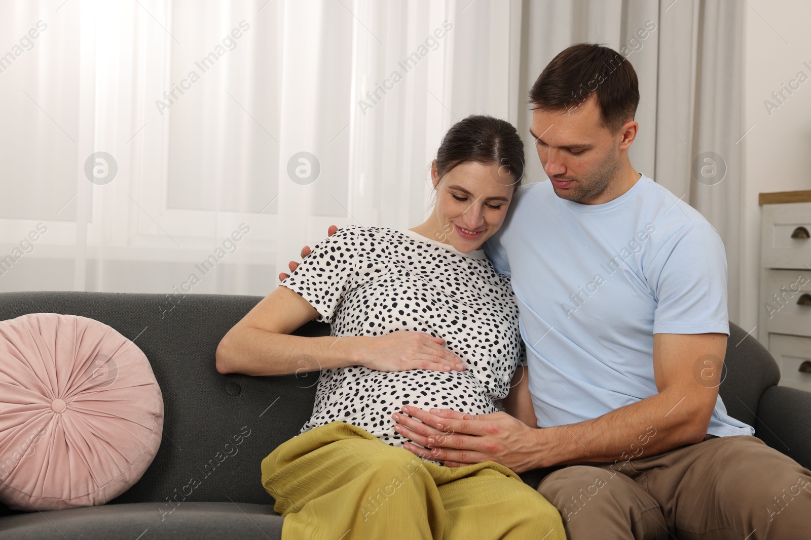 Photo of Pregnant woman and her husband on sofa at home