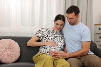 Photo of Pregnant woman and her husband on sofa at home