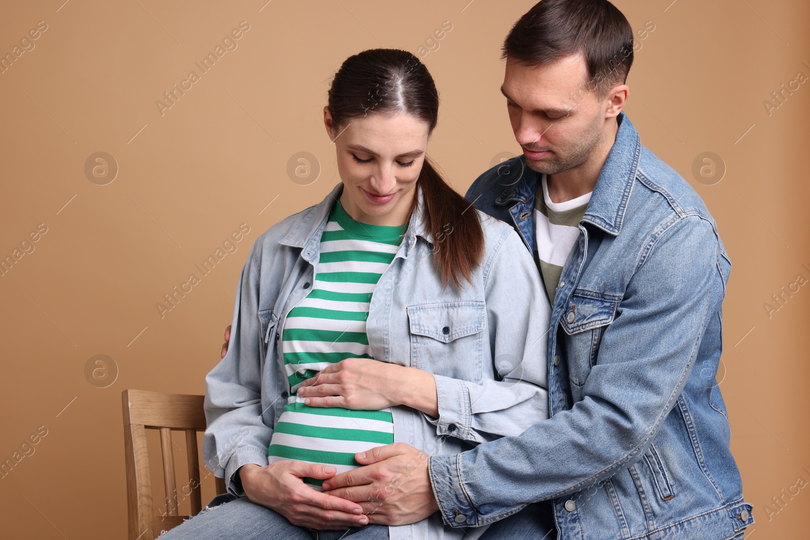 Photo of Man trying to feel baby kicks in his pregnant wife's belly on beige background