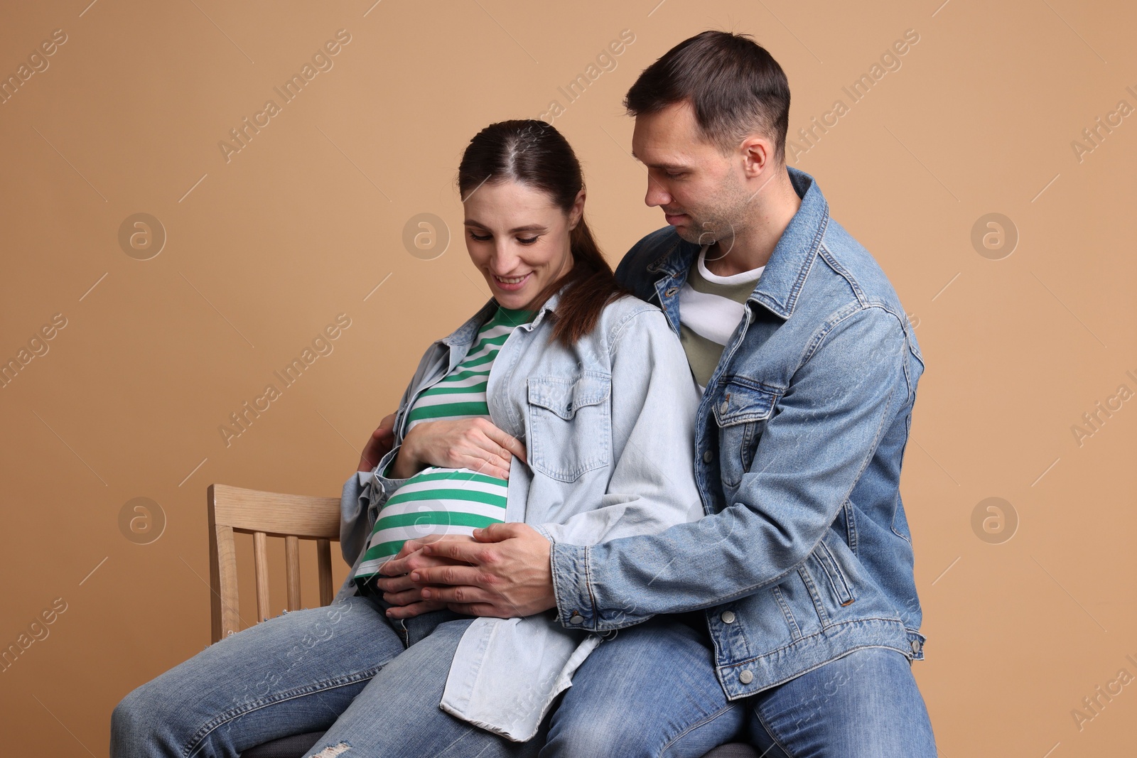 Photo of Man trying to feel baby kicks in his pregnant wife's belly on beige background