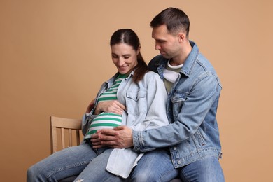 Photo of Man trying to feel baby kicks in his pregnant wife's belly on beige background